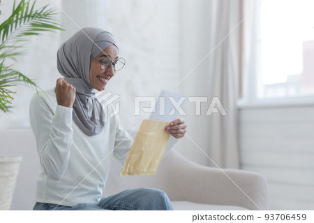 A young beautiful Muslim woman reads a happy letter home Arab student received confirmation from the university successfully passing the exam a woman in a hijab is sitting on a sofa A young beautiful Muslim woman reads a happy letter home Arab student received confirmation from the university successfully passing the exam a woman in a hijab is sitting on a sofa 93706459