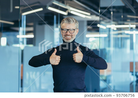 Portrait of successful businessman, senior gray-haired man in office smiling contentedly and looking at camera, investor holding affirmative thumbs up 93706756