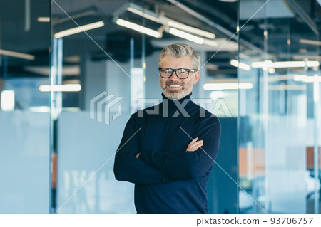 Portrait of happy gray-haired boss in glasses, businessman working in modern office standing by window smiling and looking at camera with crossed arms, satisfied investor in glasses Portrait of happy gray-haired boss in glasses, businessman working in modern office standing by window smiling and looking at camera with crossed arms, satisfied investor in glasses 93706757
