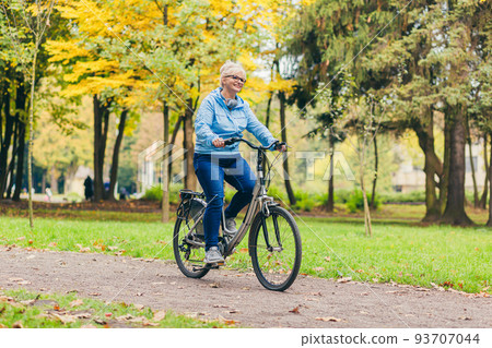 Senior beautiful blonde woman rides a bike in the park, in the woods, in nature, listens to music, spends time actively, plays sports, happy Senior beautiful blonde woman rides a bike in the park, in the woods, in nature, listens to music, spends time actively, plays sports, happy 93707044