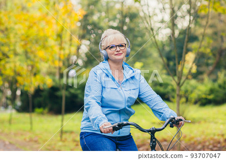 Senior beautiful blonde woman rides a bike in the park, in the woods, in nature, listens to music, spends time actively, plays sports, happy Senior beautiful blonde woman rides a bike in the park, in the woods, in nature, listens to music, spends time actively, plays sports, happy 93707047