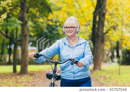 Senior beautiful blonde woman rides a bike in the park, in the woods, in nature, listens to music, spends time actively, plays sports, happy Senior beautiful blonde woman rides a bike in the park, in the woods, in nature, listens to music, spends time actively, plays sports, happy 93707048