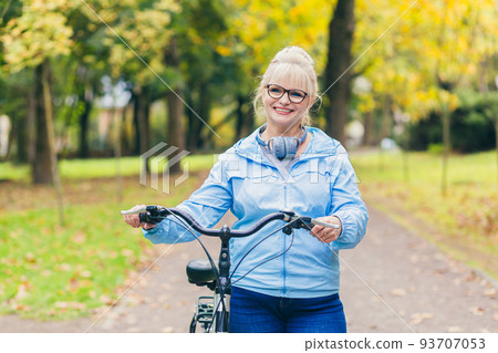 Senior beautiful blonde woman rides a bike in the park, in the woods, in nature, listens to music, spends time actively, plays sports, happy 93707053