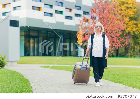 Portrait of a beautiful senior business woman walking with a suitcase near the office center 93707078