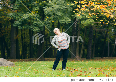 Senior woman standing and doing sports in the park on the grass, exercising, leading a healthy active lifestyle 93707123