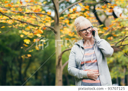 Beautiful senior woman in the park on a walk uses the phone, talking on the phone, smiling Beautiful senior woman in the park on a walk uses the phone, talking on the phone, smiling 93707125