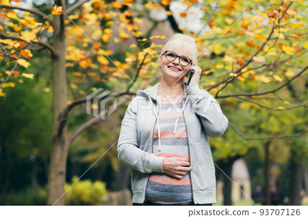 Beautiful senior woman in the park on a walk uses the phone, talking on the phone, smiling Beautiful senior woman in the park on a walk uses the phone, talking on the phone, smiling 93707126