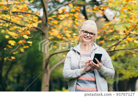 Beautiful senior woman in the park on a walk uses the phone, talking on the phone, smiling 93707127