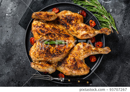 Tobacco whole chicken on plate with herbs and tomato. Black background. Top view Tobacco whole chicken on plate with herbs and tomato. Black background. Top view 93707267