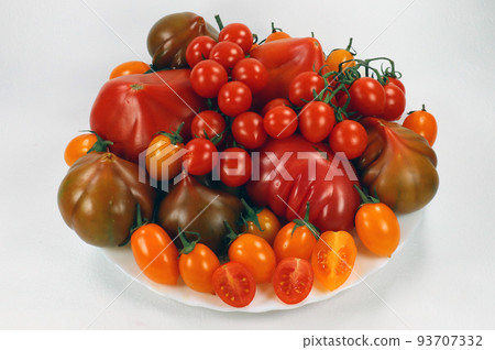 Tomatoes of different varieties, colors and shapes on a plate isolated on white. Fresh juicy appetizing Spanish tomatoes. Raf tomato, cherry, pata negro.  93707332