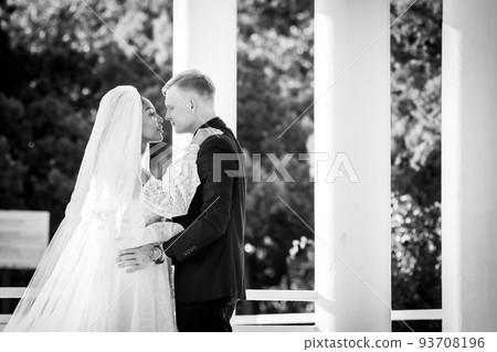 Mixed-racial newlyweds on a walk hugging and looking lovingly at each other, black and white photography 93708196