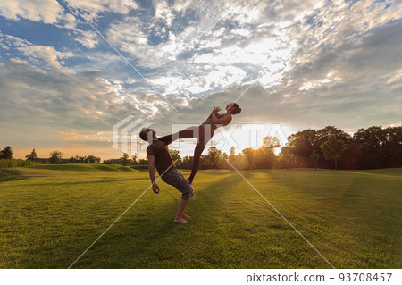 Healthy young man holds in the air a woman balancing and doing acro yoga Healthy young man holds in the air a woman balancing and doing acro yoga 93708457