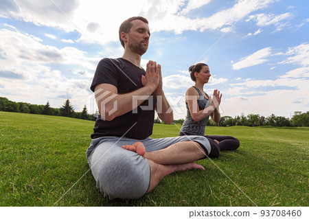 Young couple meditating in lotus position while doing yoga in park 93708460