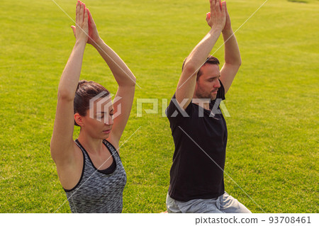 Close up of healthy man and woman doing yoga in the sunny summer park. Fitness and healthy lifestyle Close up of healthy man and woman doing yoga in the sunny summer park. Fitness and healthy lifestyle 93708461