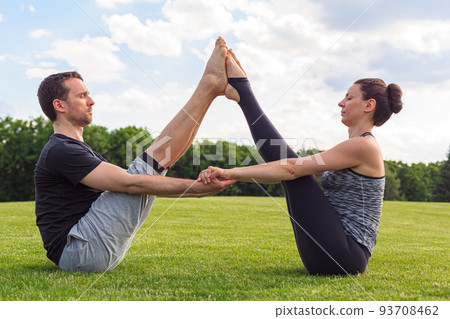 Young healthy man and woman doing yoga in the sunny summer park. Fitness and healthy lifestyle Young healthy man and woman doing yoga in the sunny summer park. Fitness and healthy lifestyle 93708462