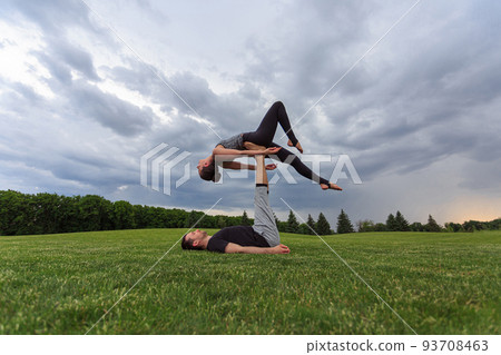 Man lying on grass and balancing woman in his feet. Young couple doing acro yoga in park Man lying on grass and balancing woman in his feet. Young couple doing acro yoga in park 93708463