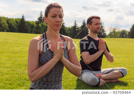Young healthy man and woman doing yoga in the sunny summer park Young healthy man and woman doing yoga in the sunny summer park 93708464