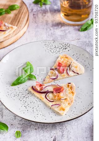 Slices French tarte flammkuchen with bacon, cream cheese and onion on a plate. Vertical view 93708720