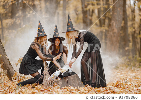 Three girls witches in forest on Halloween. Girls wearing black dresses and cone hats. Witches make a magic potion. 93708866