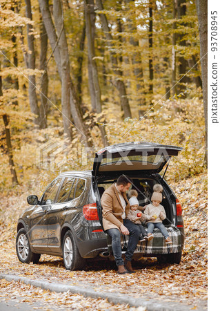 Happy family resting after day spending outdoor in autumn park. Father and two children sitting inside car trunk, smiling. Family holiday and traveling concept. Happy family resting after day spending outdoor in autumn park. Father and two children sitting inside car trunk, smiling. Family holiday and traveling concept. 93708945