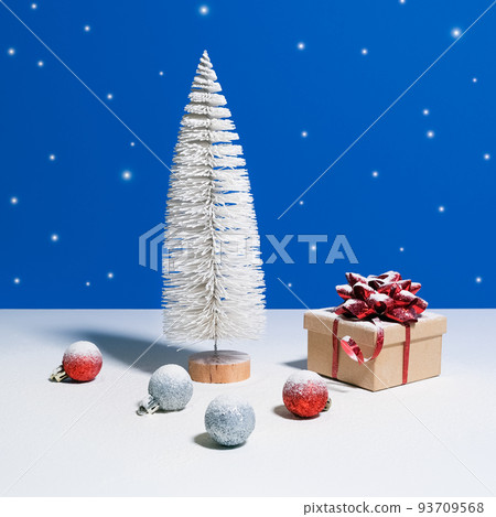Beautiful Christmas or New Year banner. Toy Christmas tree, gift box with red bow and Christmas baubles on blue background with snow falling on the background Beautiful Christmas or New Year banner. Toy Christmas tree, gift box with red bow and Christmas baubles on blue background with snow falling on the background 93709568