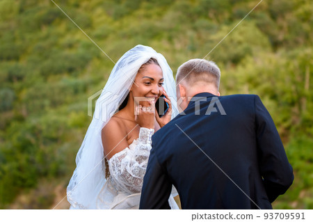 A black bride accepts congratulations on the phone and looks happily at her white husband 93709591
