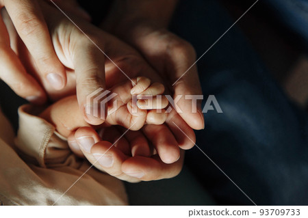 Dad and mom hold in their palms the gentle little hand of their newborn baby. 93709733