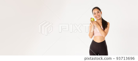 Sport, wellbeing and active lifestyle concept. Smiling cute asian fitness coach, girl athlete in sportswear showing green apple, sit on diet and workout to gain perfect body, white background Sport, wellbeing and active lifestyle concept. Smiling cute asian fitness coach, girl athlete in sportswear showing green apple, sit on diet and workout to gain perfect body, white background 93713696