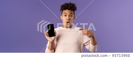 Close-up portrait of excited, cheerful young hispanic male geek talking about his device, new gadget or application, holding mobile phone, pointing at smartphone with amused face 93713908