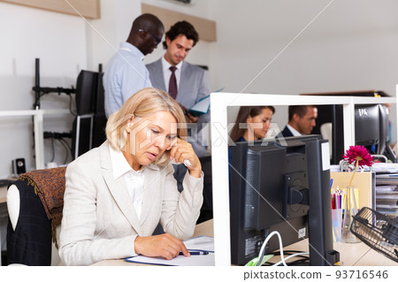 Upset mature woman sitting at desk in open plan office Upset mature woman sitting at desk in open plan office 93716546