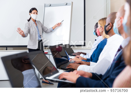 Asian woman business coach in protective mask lecturing to businesspeople Asian woman business coach in protective mask lecturing to businesspeople 93716700