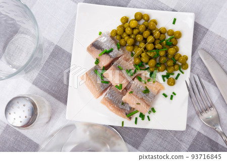 Tasty slices herring fillet with canned green peas served on plate 93716845