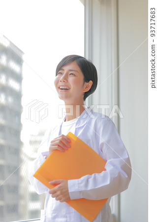 窗邊拿著文件微笑的白大褂女人_Vertical 3 窗邊拿著文件微笑的白大褂女人_Vertical 3 93717683