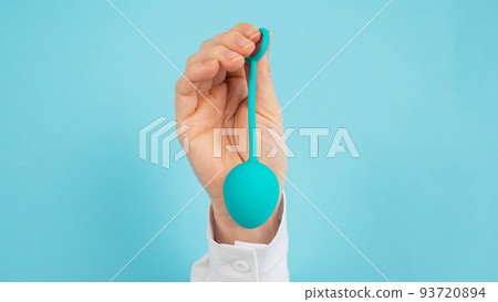 A woman's hand sticks out of a hole in a blue background and holds a vaginal egg. A woman's hand sticks out of a hole in a blue background and holds a vaginal egg. 93720894
