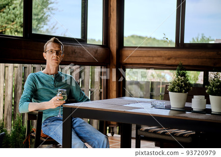 Man is resting on the veranda with a glass of wine 93720979
