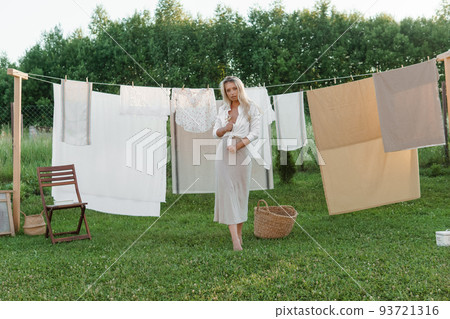 Laundry day. A woman hangs linen and towels on a tree in the courtyard of a village house. Laundry day. A woman hangs linen and towels on a tree in the courtyard of a village house. 93721316