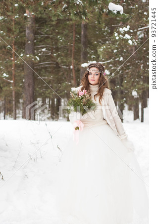 Beautiful bride in a white dress with a bouquet in a snow-covered winter forest. Portrait of the bride in nature Beautiful bride in a white dress with a bouquet in a snow-covered winter forest. Portrait of the bride in nature 93721445