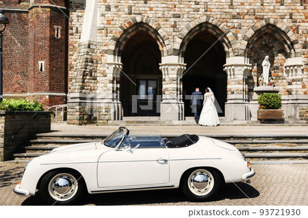 Newlyweds are walking up the stairs of the church and old white car Newlyweds are walking up the stairs of the church and old white car 93721930