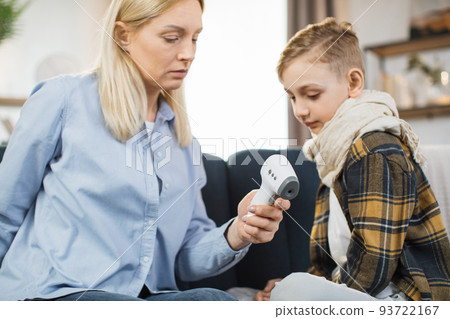 Mother taking care of her cute sick teen boy suffering from cold, checking temperature 93722167