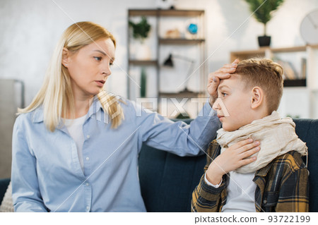 Mother taking care of her cute sick teen boy suffering from cold while touching his forehead Mother taking care of her cute sick teen boy suffering from cold while touching his forehead 93722199