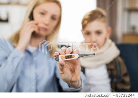 Mom checking temperature of her sick teen son with high fever sitting on sofa. 93722244
