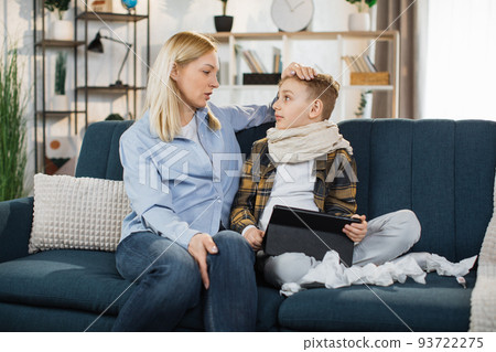 Mother spending time together with her sick teen son, sitting on the sofa and using tablet pc. Mother spending time together with her sick teen son, sitting on the sofa and using tablet pc. 93722275