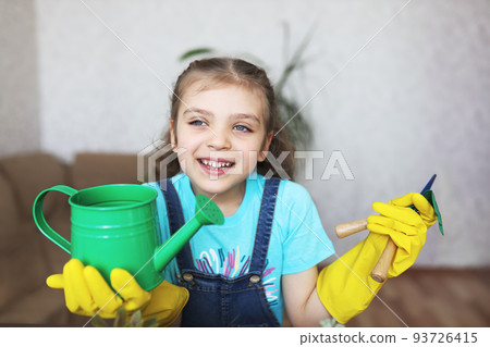 girl in blue t-shirt and yellow gloves with green watering can and gardening tools home girl in blue t-shirt and yellow gloves with green watering can and gardening tools home 93726415