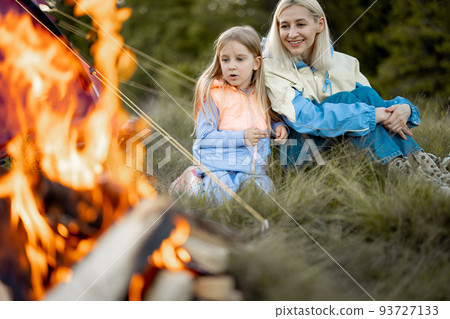 Mother with daughter sit by the campfire near tent on nature Mother with daughter sit by the campfire near tent on nature 93727133