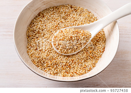Toasted sesame seeds and white spoon in a porcelain bowl. 93727438