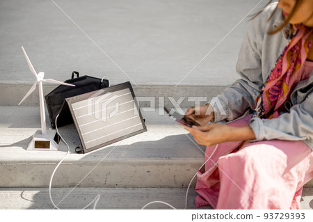 Woman charge phone from a portable solar panel 93729393