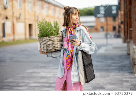 Woman charge phone from portable solar panel while walking outdoors 93730372