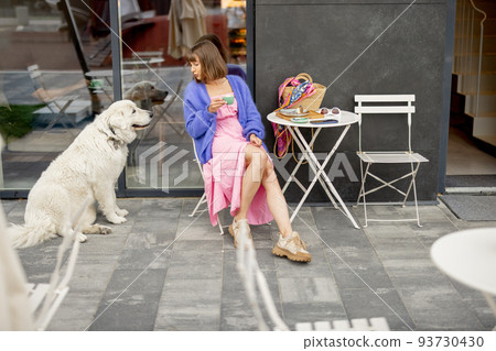 Woman sits with her adorable white dog at cafe on a street 93730430