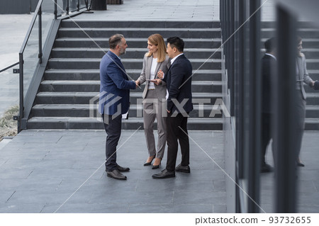 Meeting of three successful business people, diverse dream team man and woman outside office building, greeting and shaking hands, experienced professionals specialists in business suits talking Meeting of three successful business people, diverse dream team man and woman outside office building, greeting and shaking hands, experienced professionals specialists in business suits talking 93732655