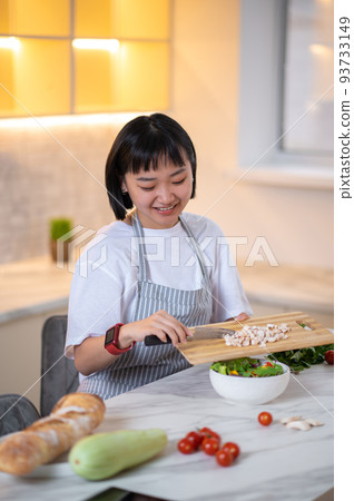 A woman making salad from fresh vegetables in the kitchen A woman making salad from fresh vegetables in the kitchen 93733149